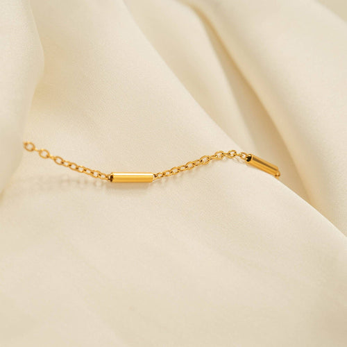 Gold bar and chain necklace on a beige fabric background