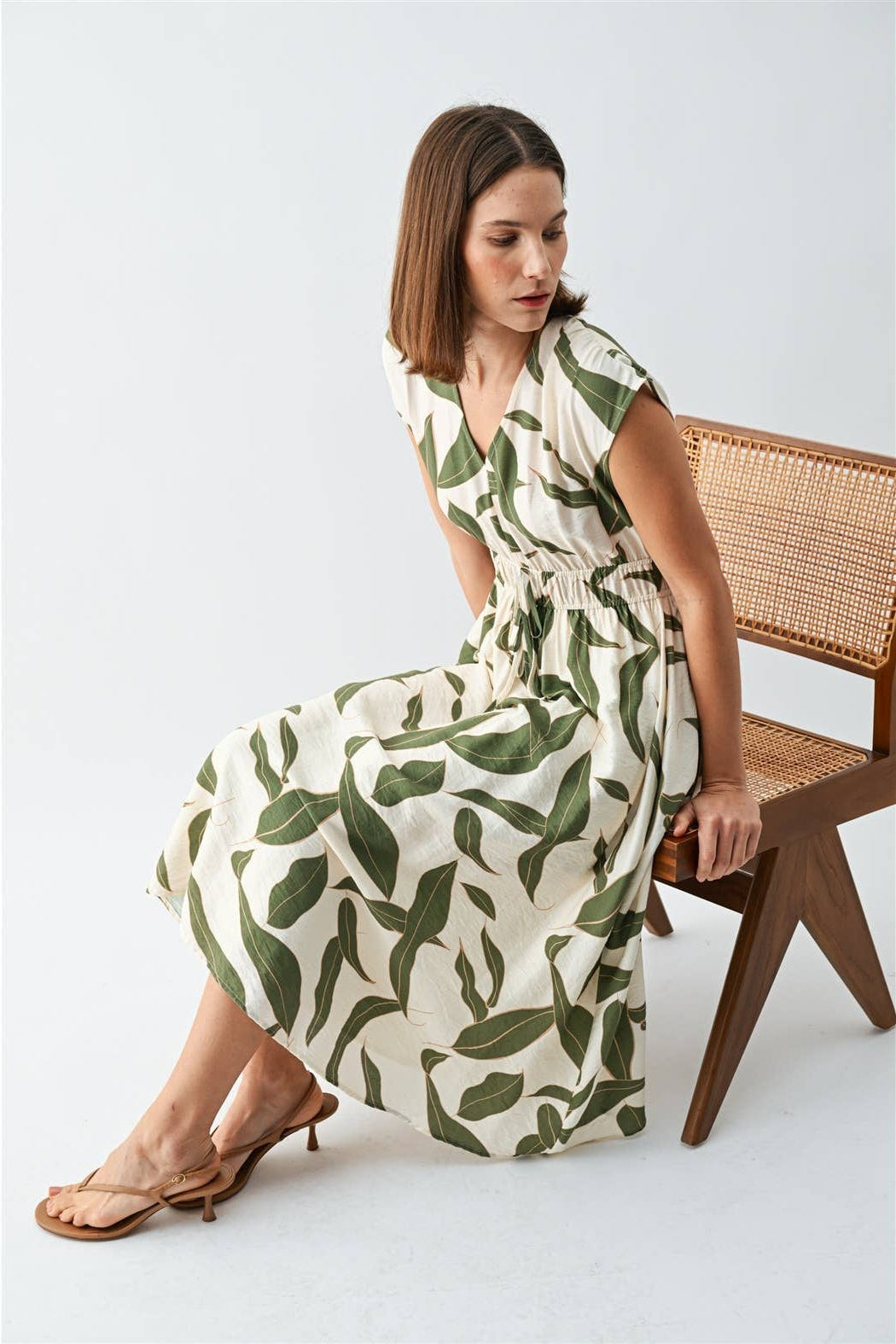 Woman wearing a green leaf-patterned dress sitting on a wooden chair.