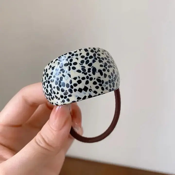 Woman's black and cream patterned hair tie against a plain background