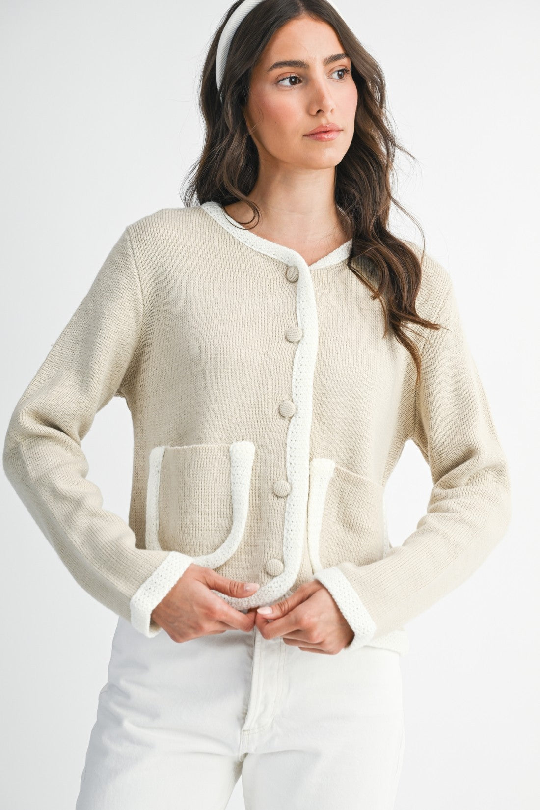 Woman wearing a lt. taupe and ivory cardigan  and white pants on a plain background