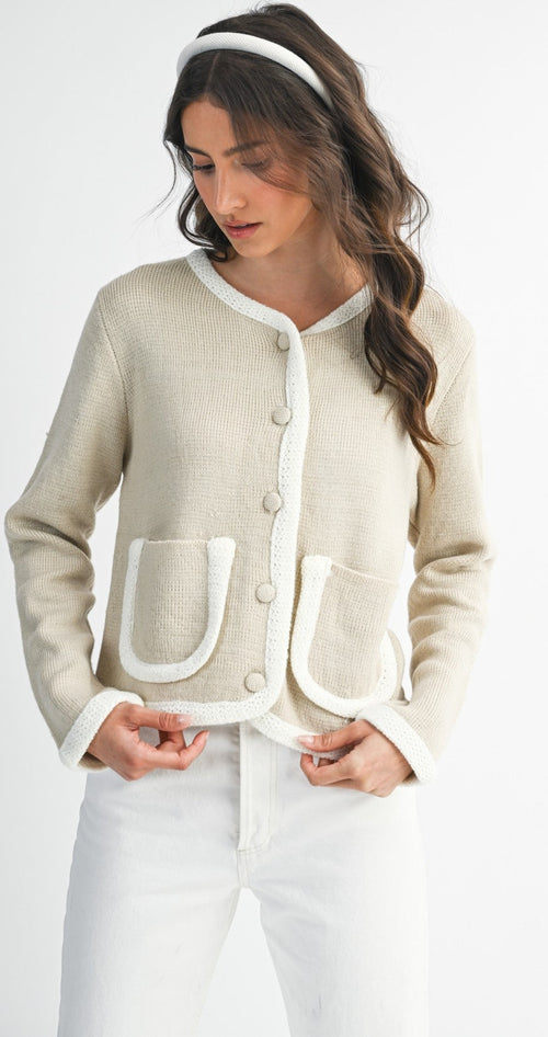 Woman wearing a light taupe and ivory cardigan  and white pants on a plain background