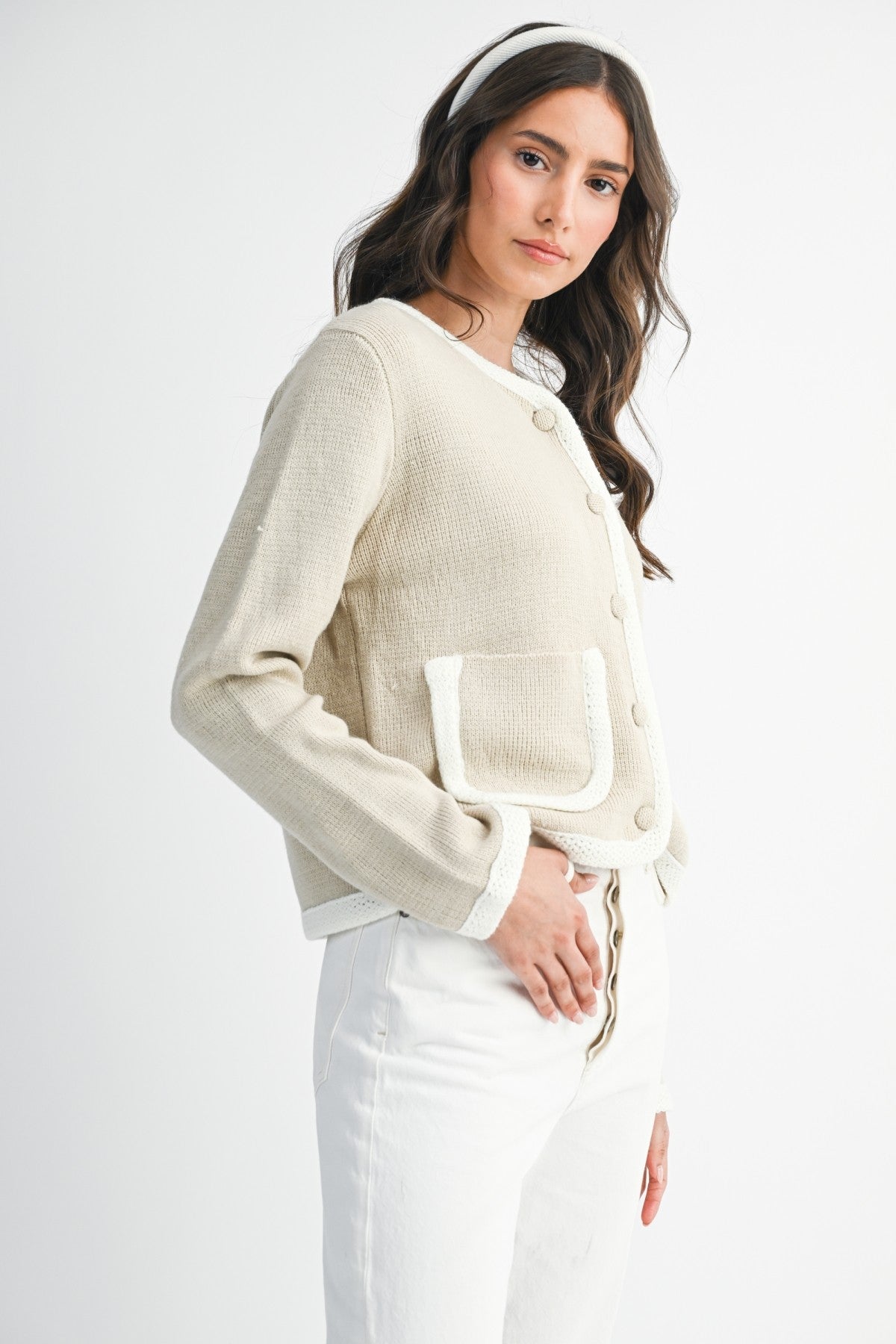 Woman wearing a lt. taupe and ivory cardigan  and white pants on a plain background