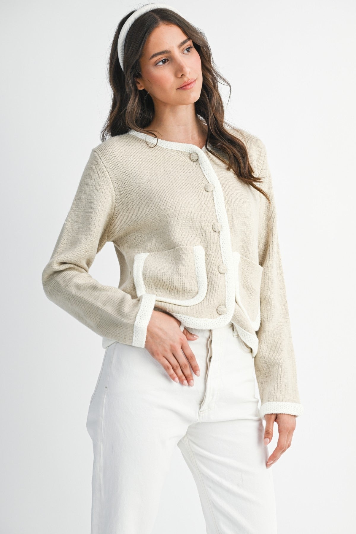 Woman wearing a lt. taupe and ivory cardigan  and white pants on a plain background