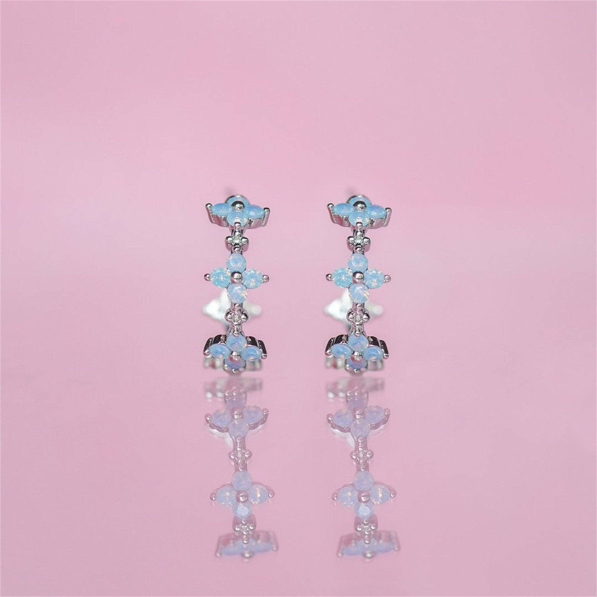 Pair of floral earrings with blue and silver details on a pink background