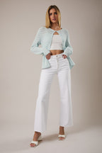 Woman wearing open weave button pale aqua pointelle knit cardigan over white tank and white jeans on a neutral background