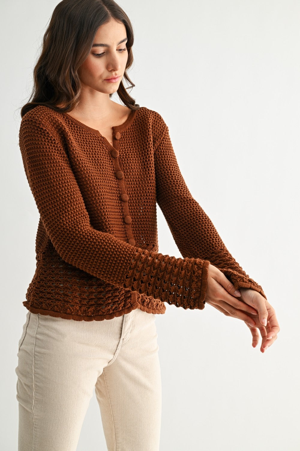 Woman wearing a chocolate brown knitted sweater with crochet detailing on a white background