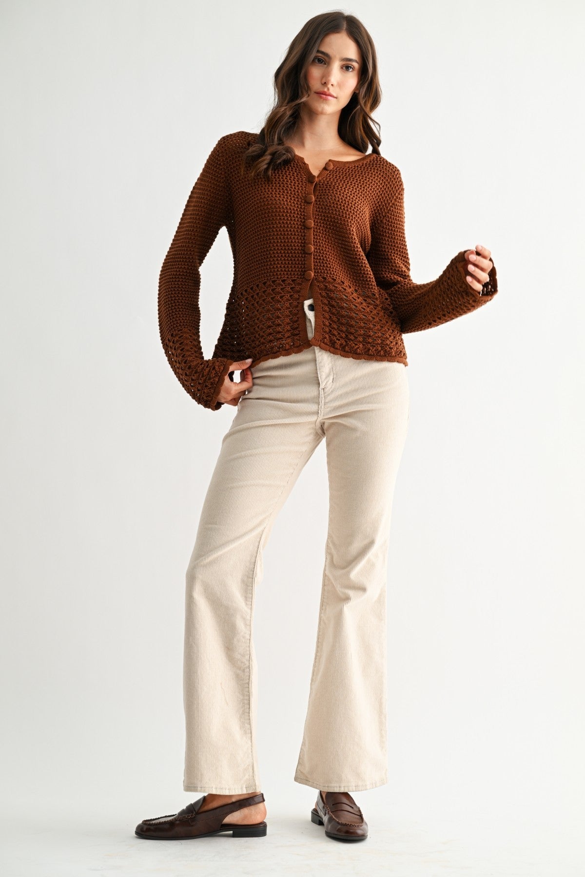 Woman wearing a chocolate brown knitted cardigan and beige pants on a white background