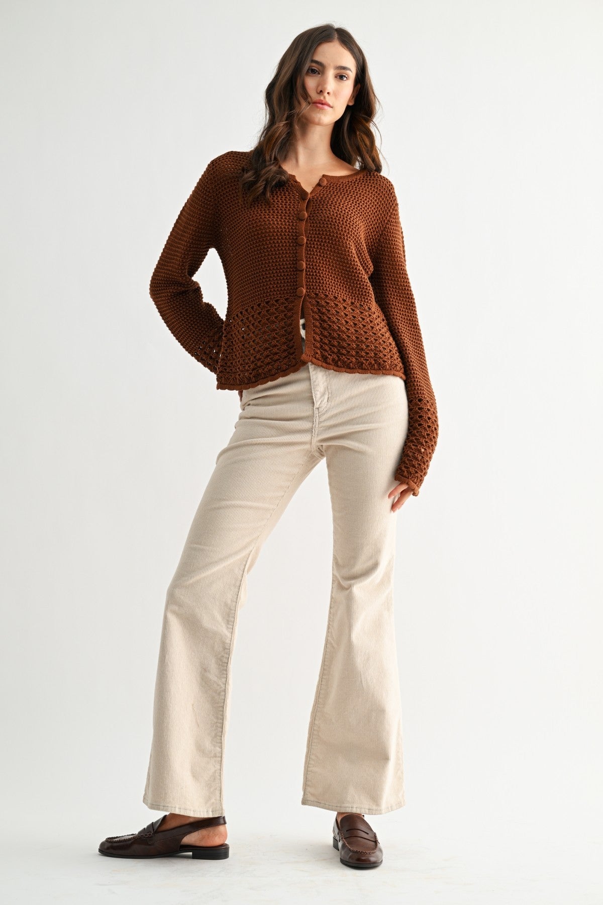 Woman wearing a chocolate brown knitted cardigan and beige pants on a white background
