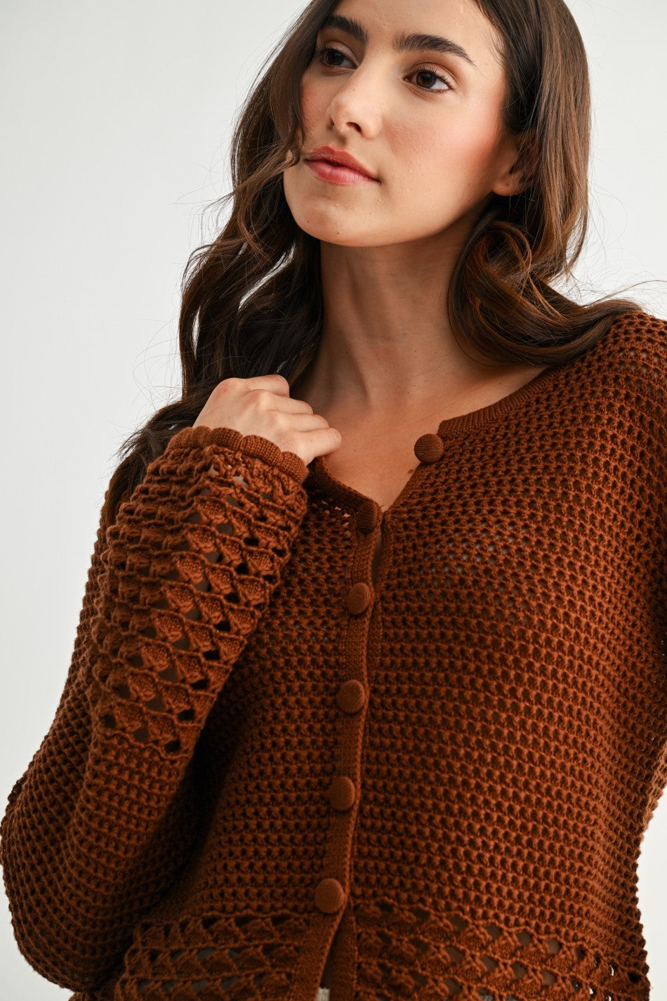 Woman wearing a chocolate brown crochet detail cardigan against a plain background