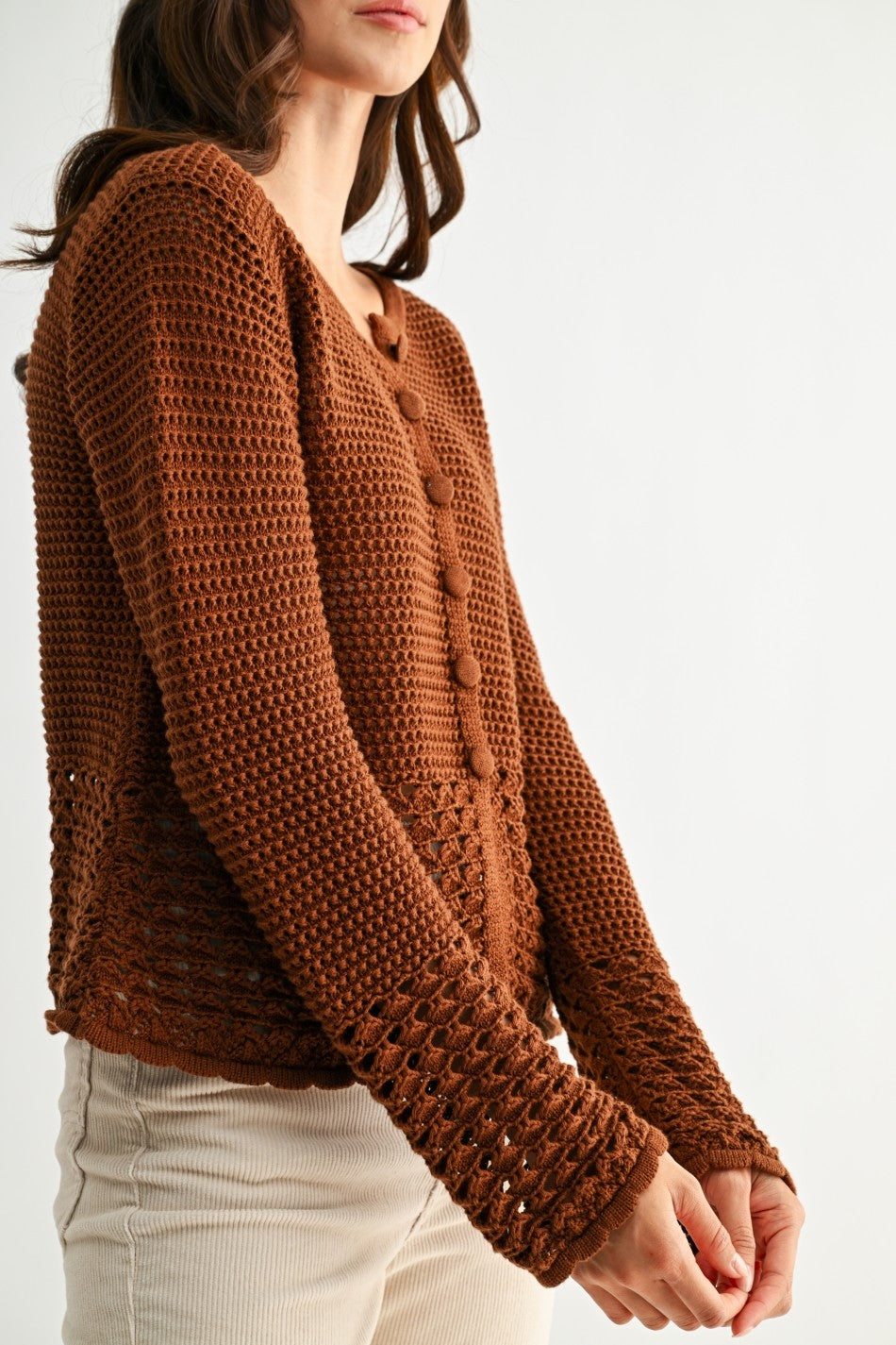 Woman wearing a chocolate brown knitted cardigan with crochet detailing on a white background