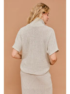 Back view of woman wearing natural textured knit turtle neck short sleeve top on a beige background