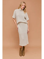 Woman wearing natural textured knit turtle neck short sleeve top and matching midi skirt on a beige background