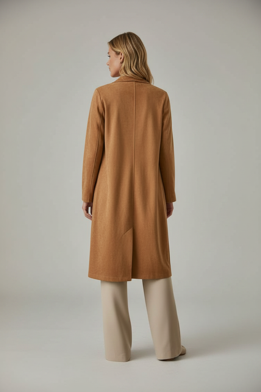 Back view of a woman wearing a long camel faux suede coat over a white top and tan pants against cream background
