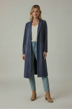 A woman wearing a long navy faux suede coat over a white top and light jeans against a grey background