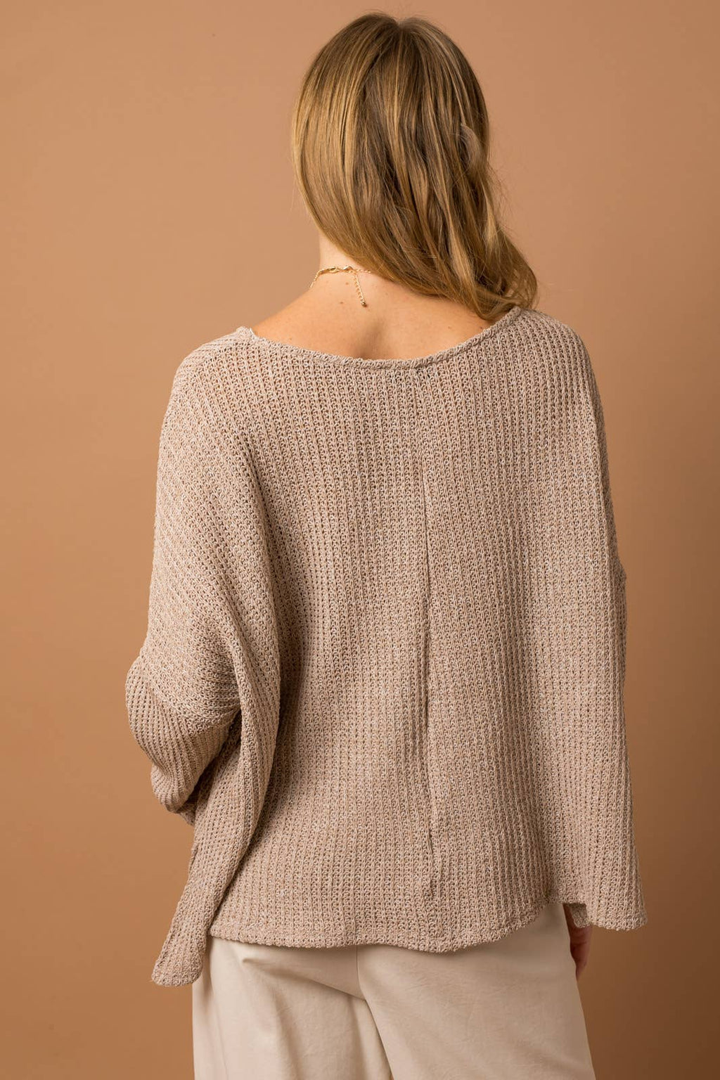 Woman wearing a taupe woven top showing back center seam detail against a brown background