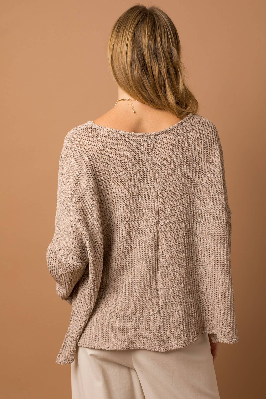 Woman wearing a taupe woven top showing back center seam detail against a brown background