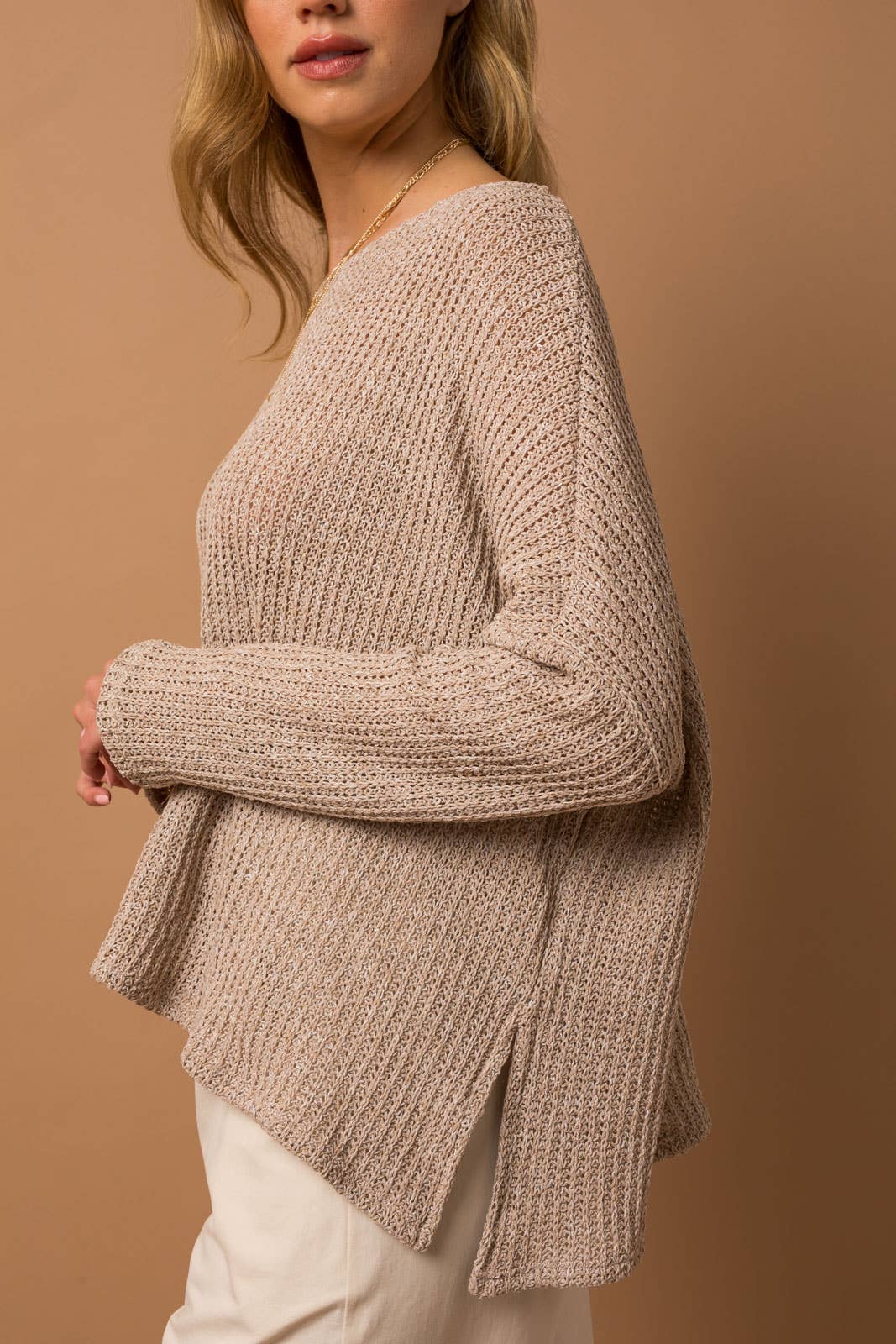 Woman wearing taupe woven top with side slits on a brown background