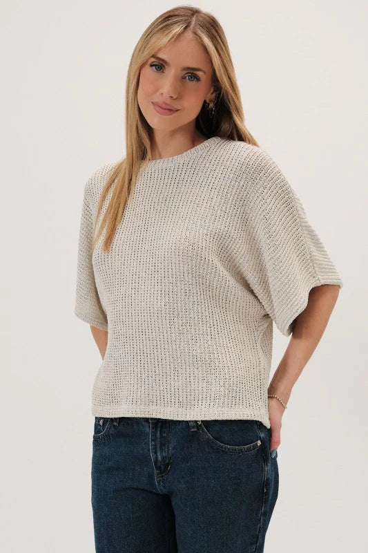 Woman wearing a natural boucle knit sweater and dark jeans on a white background