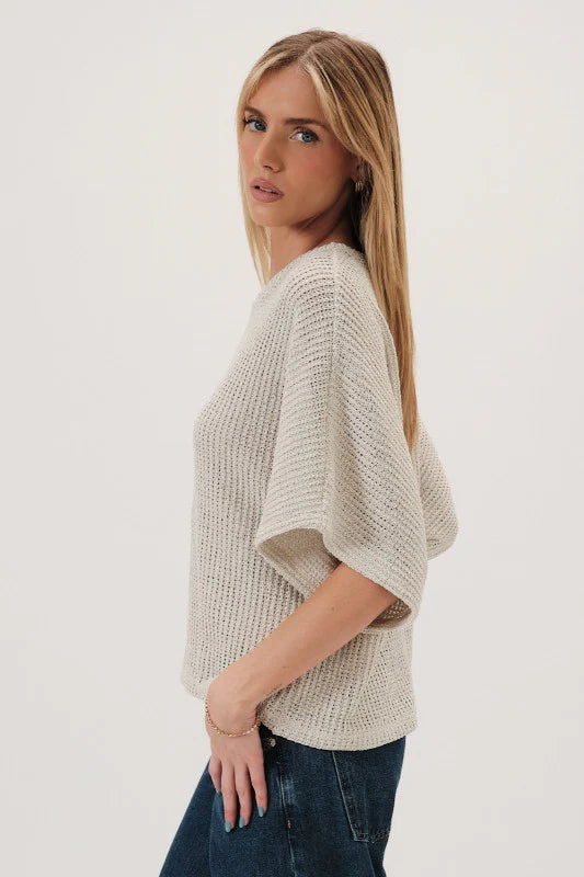 Woman wearing a natural boucle knit sweater and dark jeans on a white background