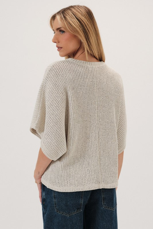Back view of a woman wearing a natural boucle knit sweater and dark jeans on a white background