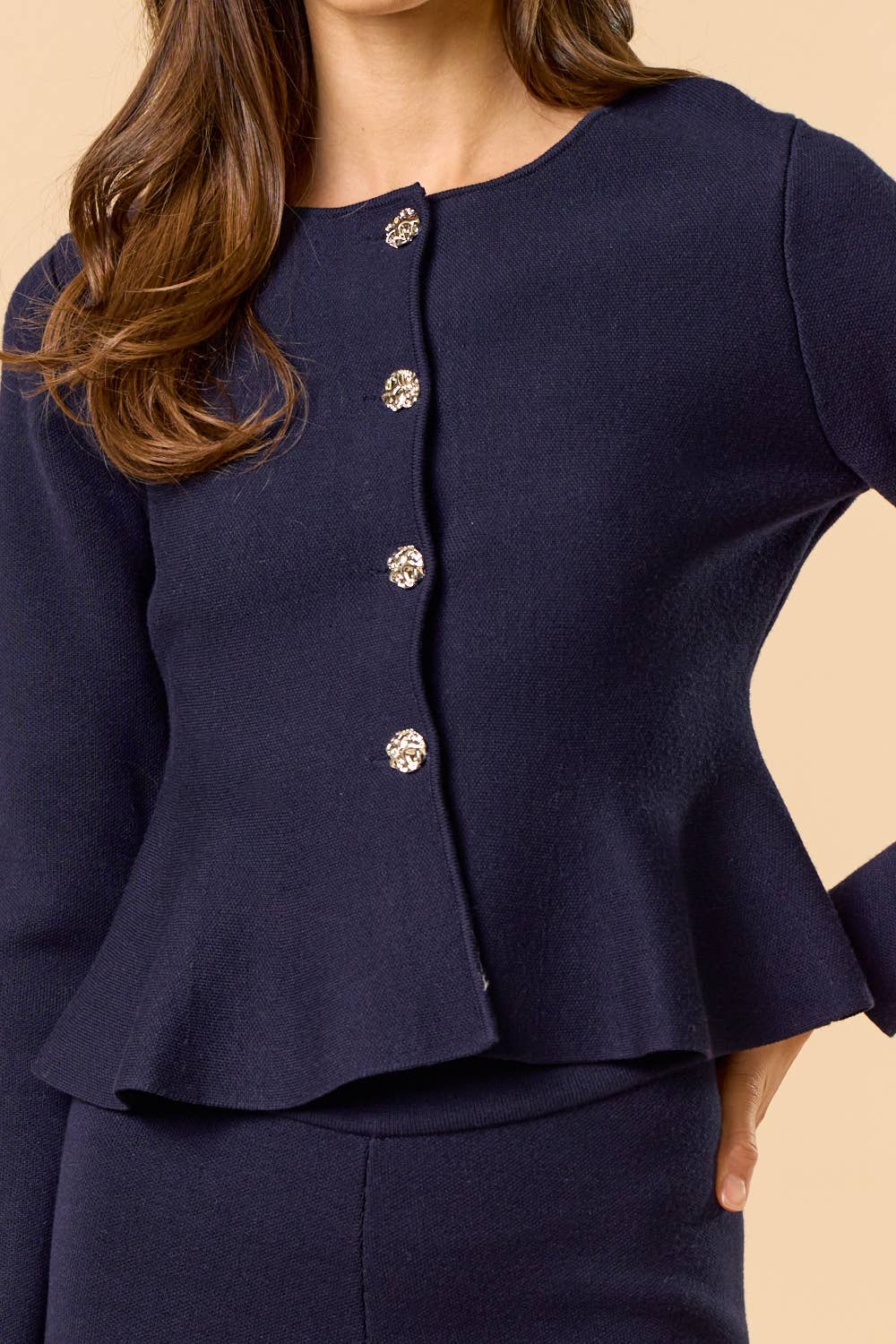 Woman wearing navy peplum cardigan with silver buttons on tan backgrouond