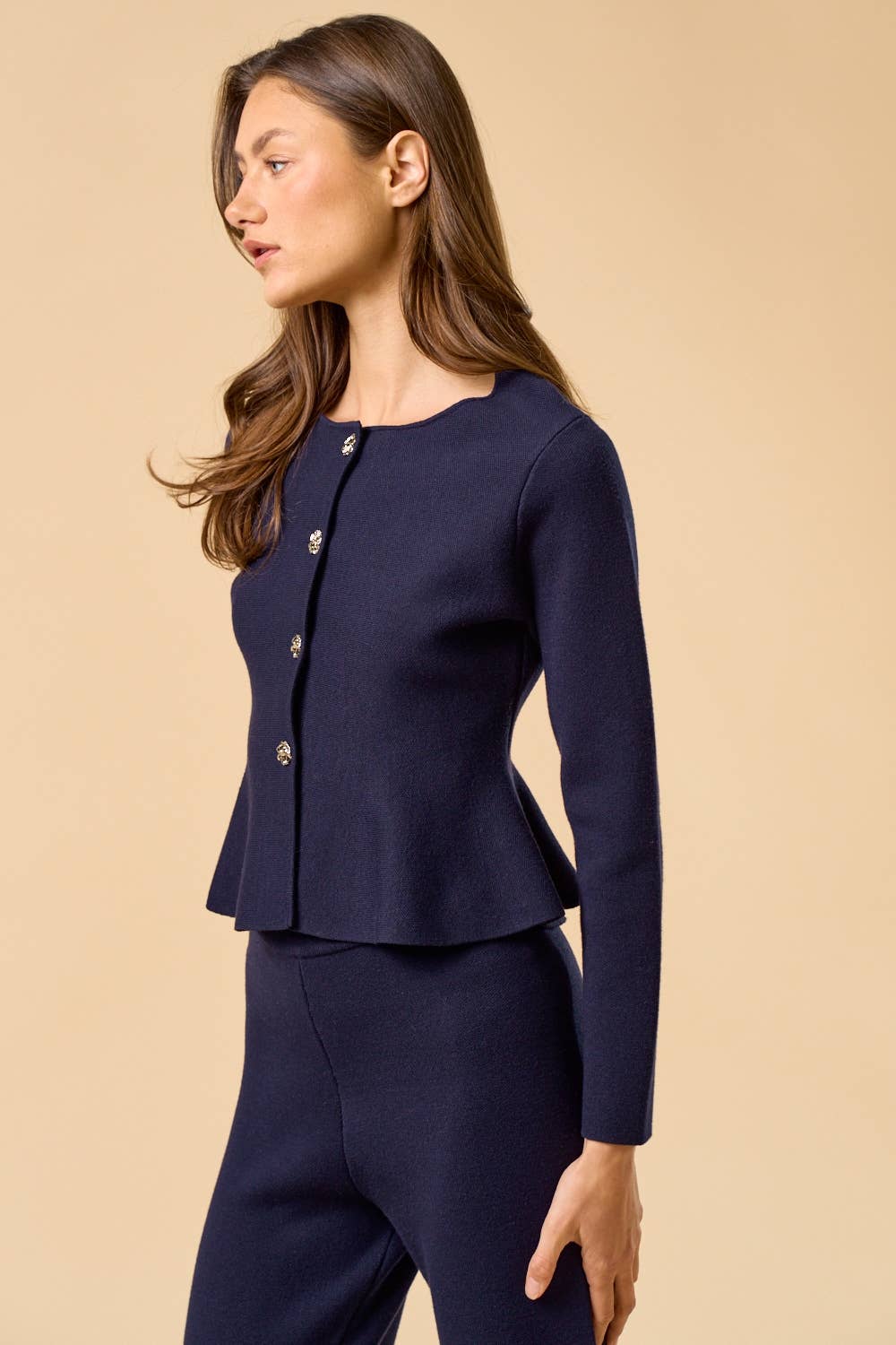 Woman wearing navy peplum cardigan with silver buttons on tan backgrouond