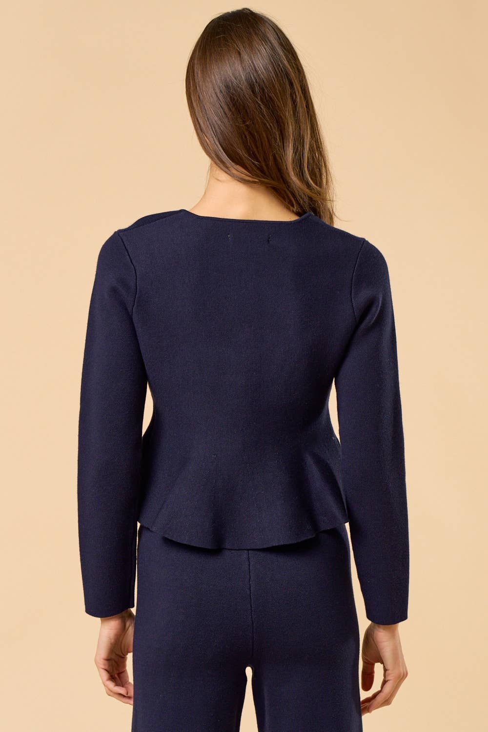 View from back of woman wearing navy peplum cardigan on a tan background