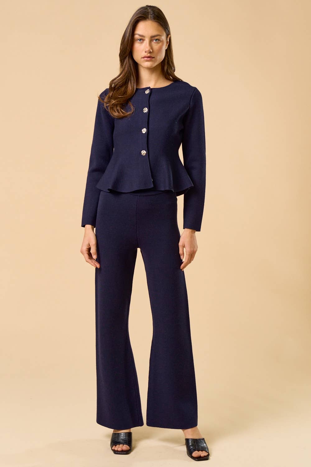 Woman wearing a navy peplum cardigan and navy pants on a beige background