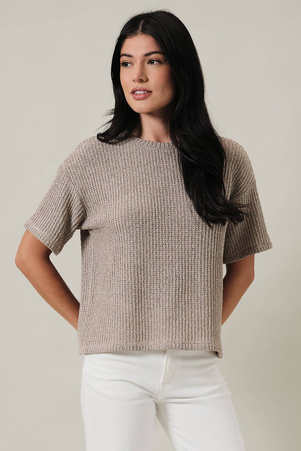 Woman wearing an oatmeal boucle knit top and white pants against a plain background