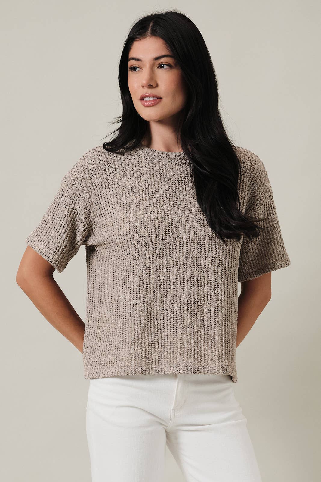 Woman wearing an oatmeal boucle knit top and white pants against a plain background
