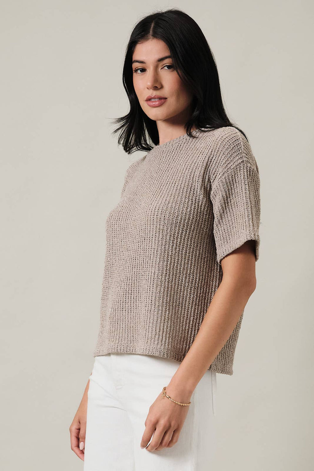 Woman wearing an oatmeal boucle knit top and white pants against a plain background