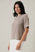 Woman wearing an oatmeal boucle knit top and white pants against a plain background