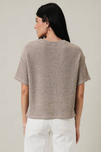 Back view of a woman wearing an oatmeal boucle knit top and white pants against a plain background