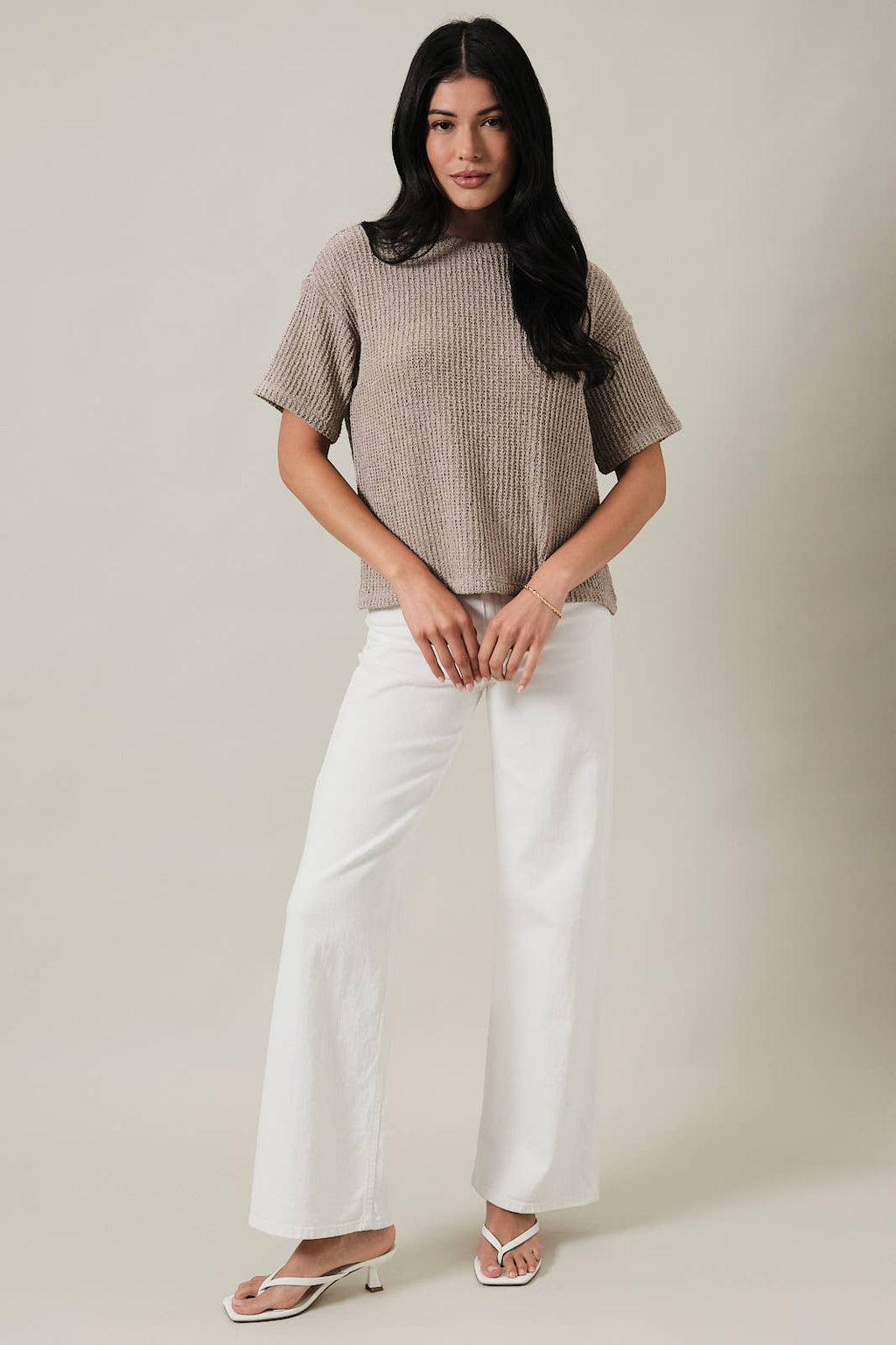 Woman wearing an oatmeal boucle knit top and white pants against a plain background