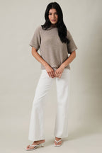 Woman wearing an oatmeal boucle knit top and white pants against a plain background