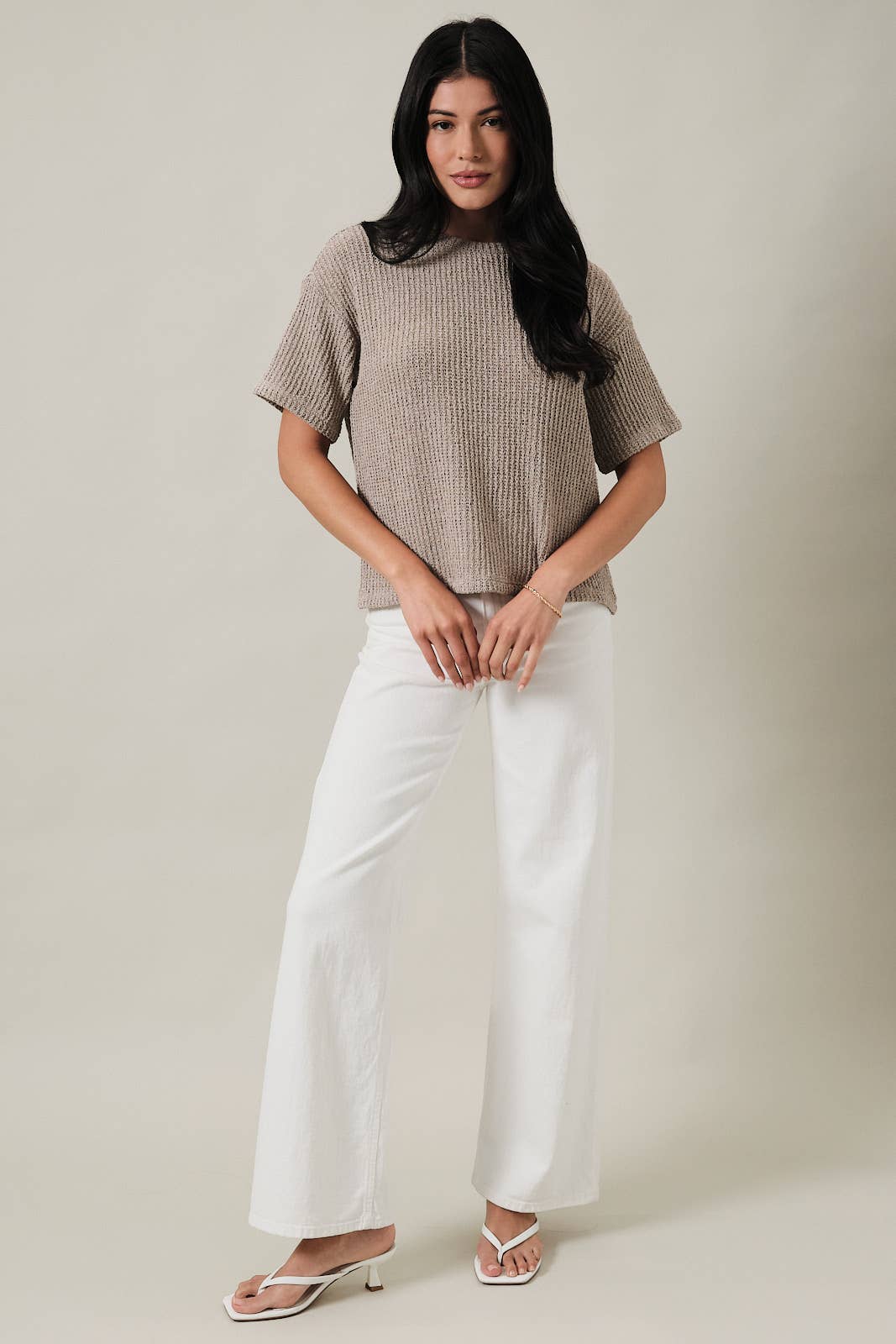 Woman wearing an oatmeal boucle knit top and white pants against a plain background
