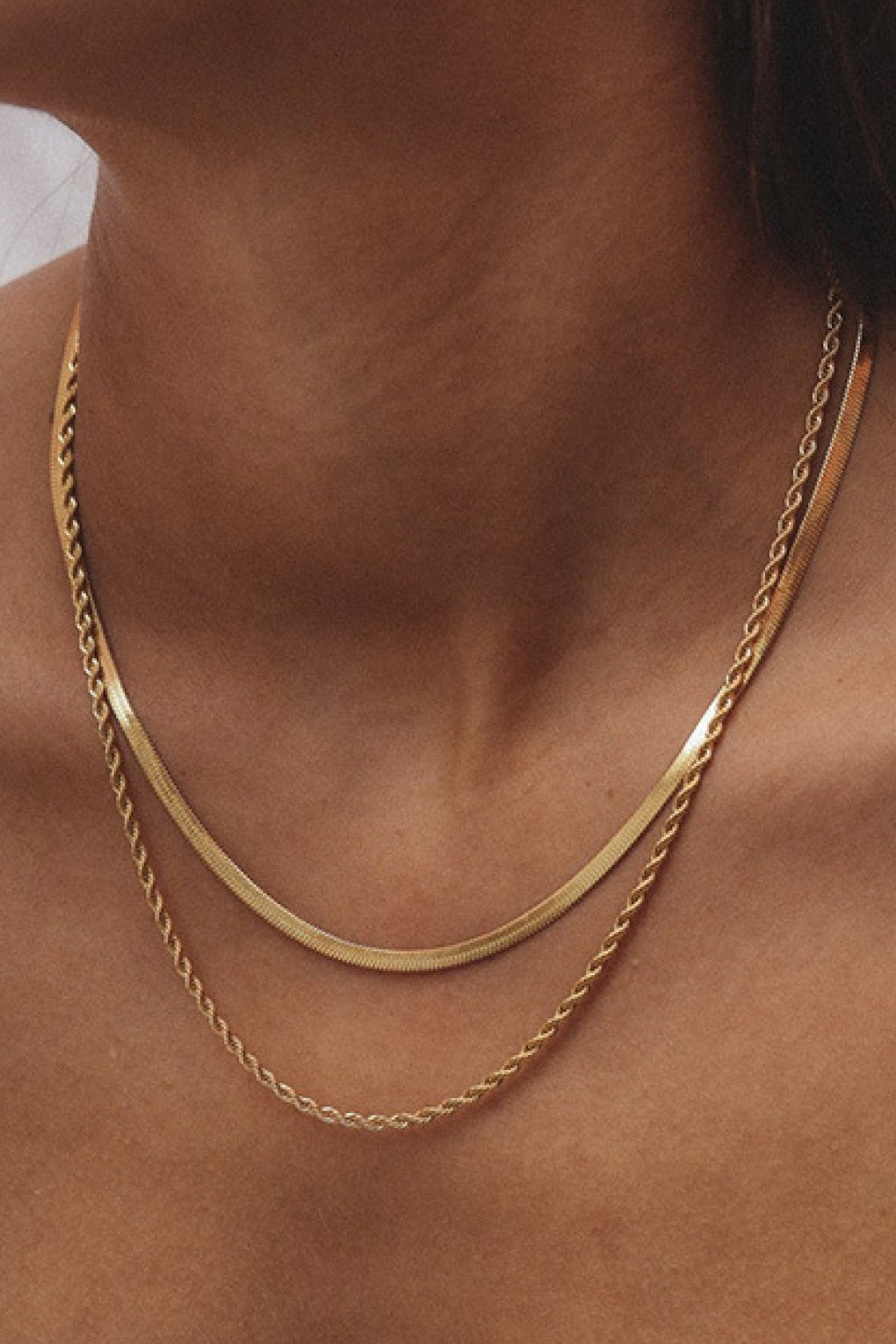 Women's gold link chain and snake necklace on a person's neck