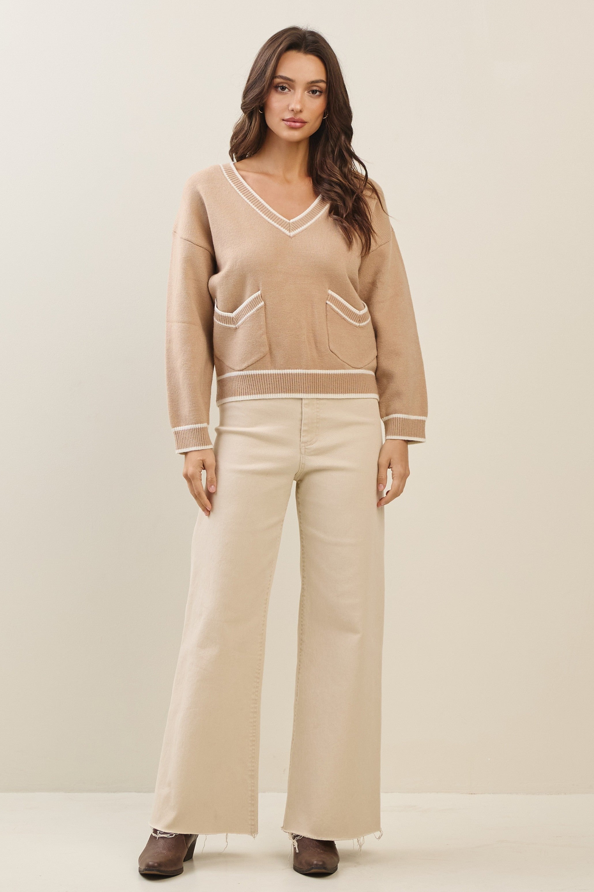 Woman wearing a tan varsity sweater with contrasting white stripe and pants set on a plain background
