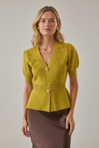 Woman wearing a chartreuse knit peplum cardigan and brown skirt against a white brick wall background