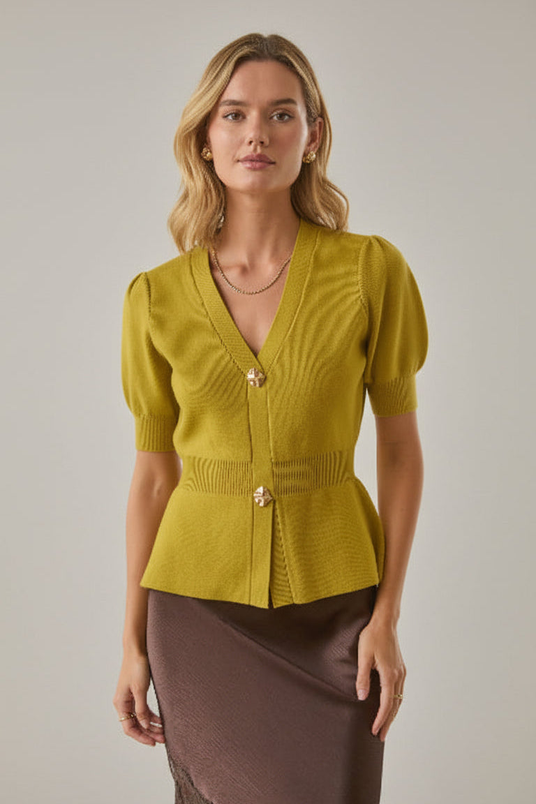 Woman wearing a chartreuse knit peplum cardigan and brown skirt against a white brick wall background