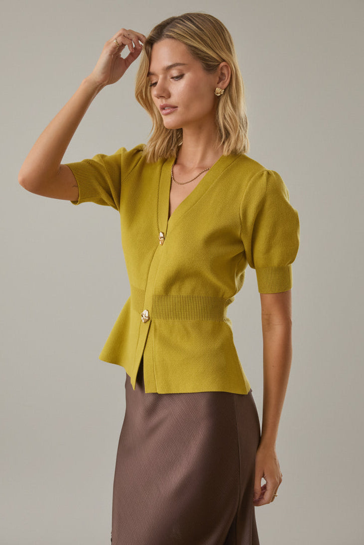 Woman wearing a chartreuse knit peplum cardigan and brown skirt against a white brick wall background