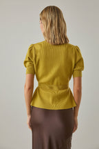 Back view of a woman wearing a chartreuse knit peplum cardigan and brown skirt against a white brick wall backgroundB