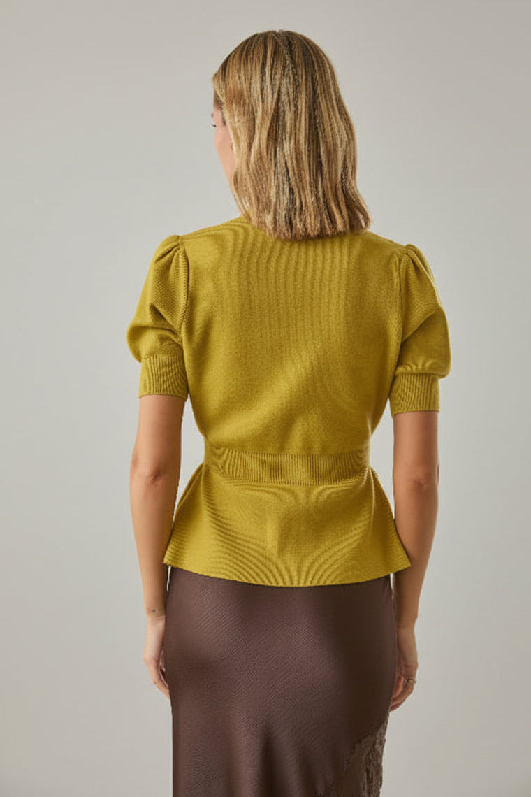 Back view of a woman wearing a chartreuse knit peplum cardigan and brown skirt against a white brick wall backgroundB