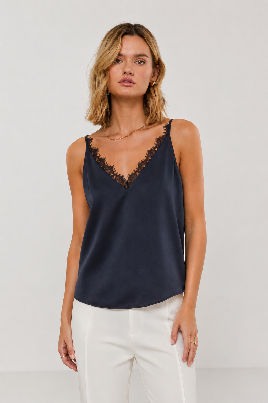 Woman wearing a navy sleeveless tank with lace trim and white pants on a light gray background