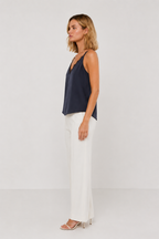 Woman wearing a navy sleeveless tank and white pants on a light gray background