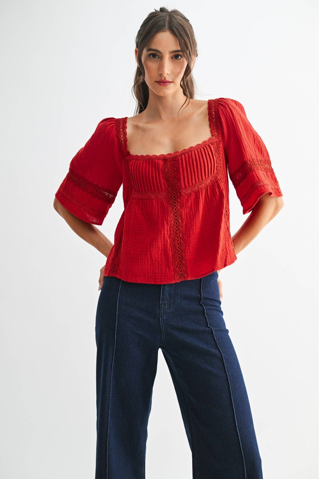 Woman wearing a scarlet lace and pleated detail top and blue jeans on a white background
