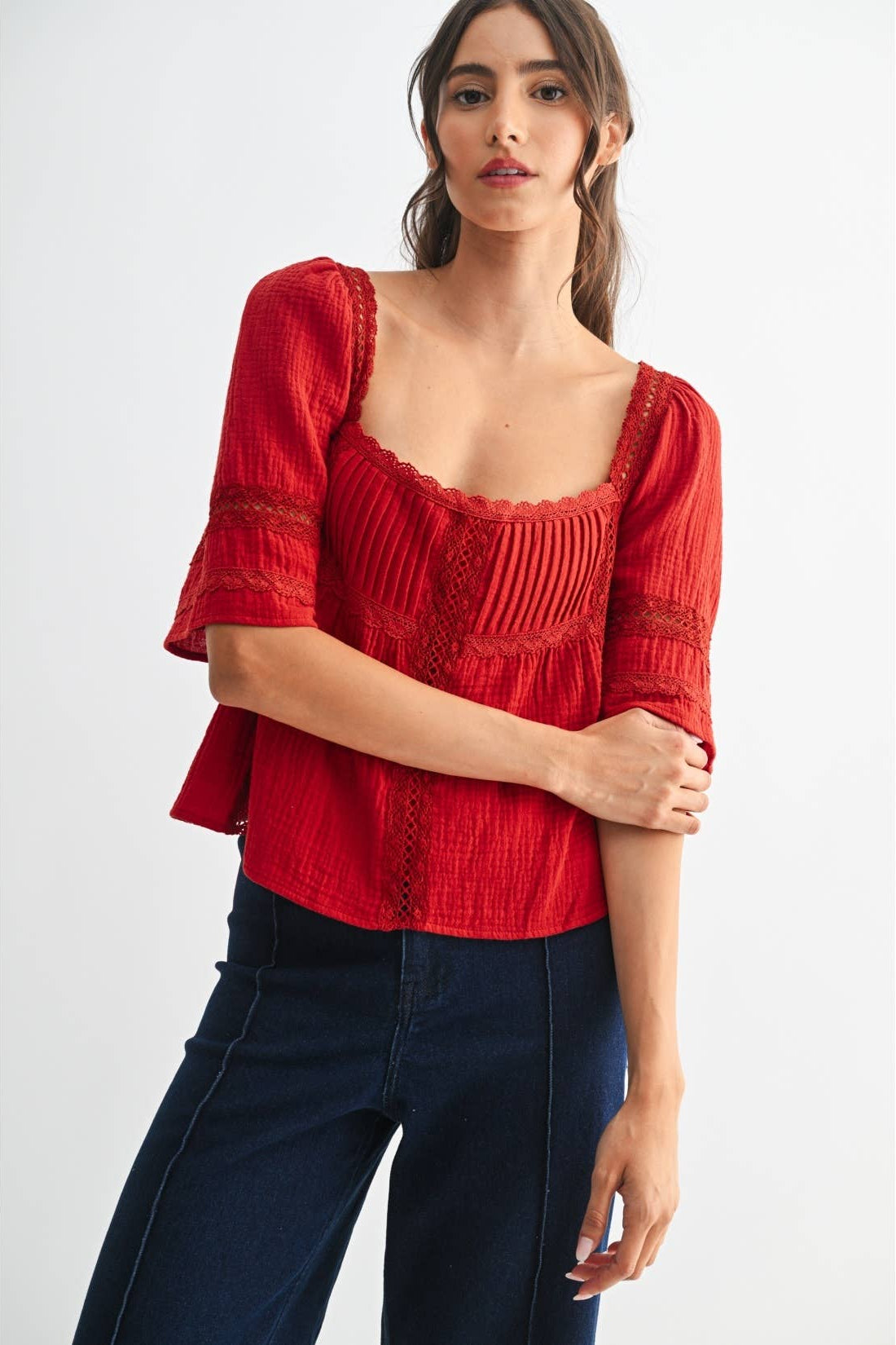 Woman wearing a scarlet lace and pleated detail top and blue jeans on a white background