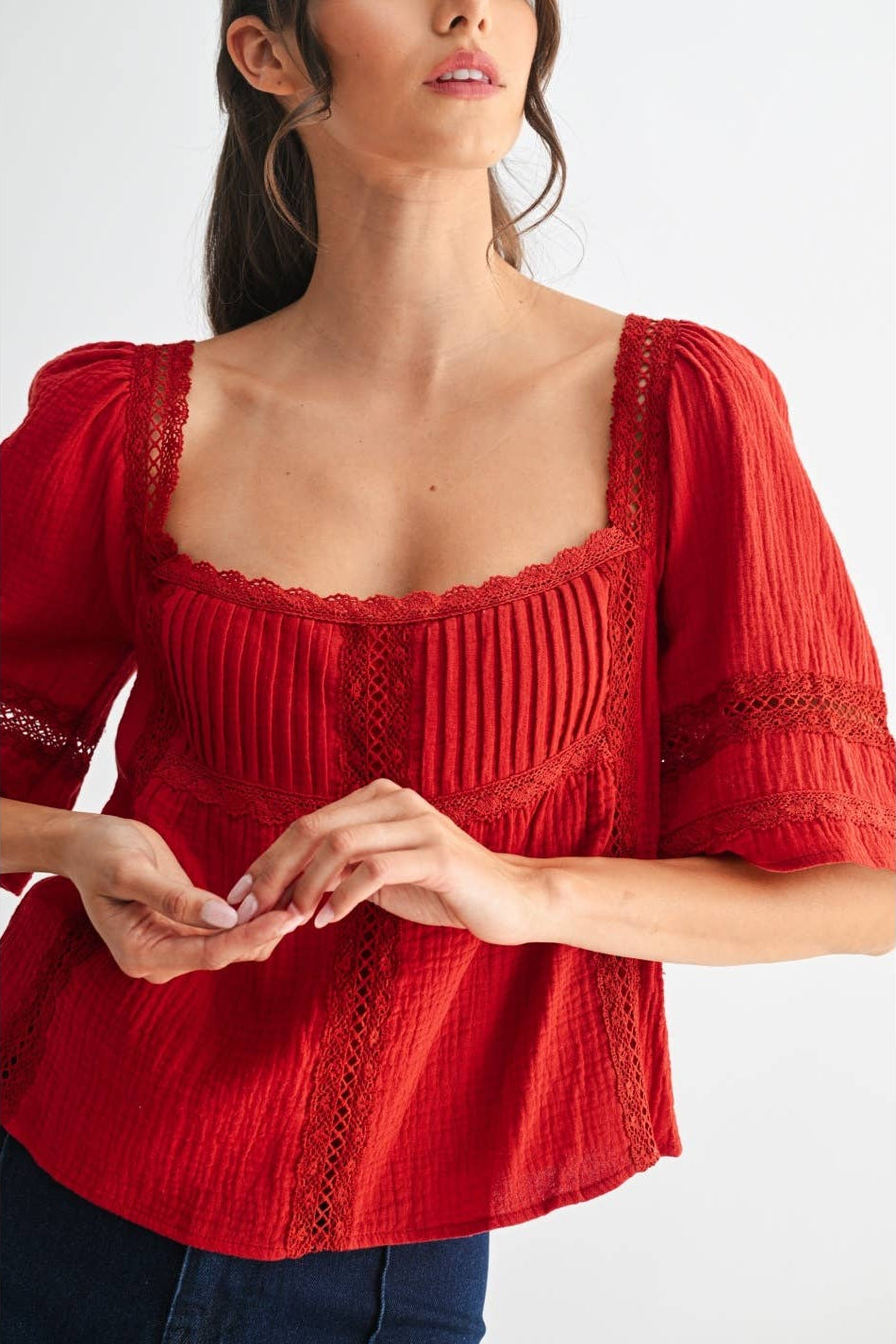 Woman wearing a scarlet lace and pleated detail top and blue jeans on a white background