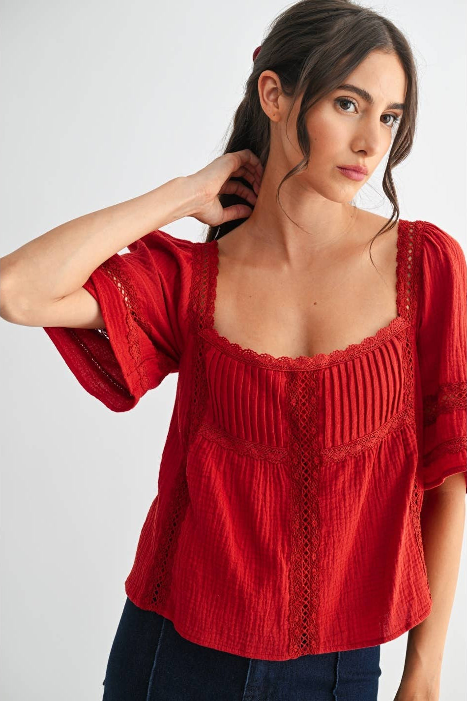 Woman wearing a scarlet lace and pleated detail top and blue jeans on a white background