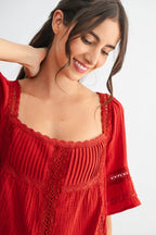 Woman wearing a scarlet lace and pleated detail top and blue jeans on a white background